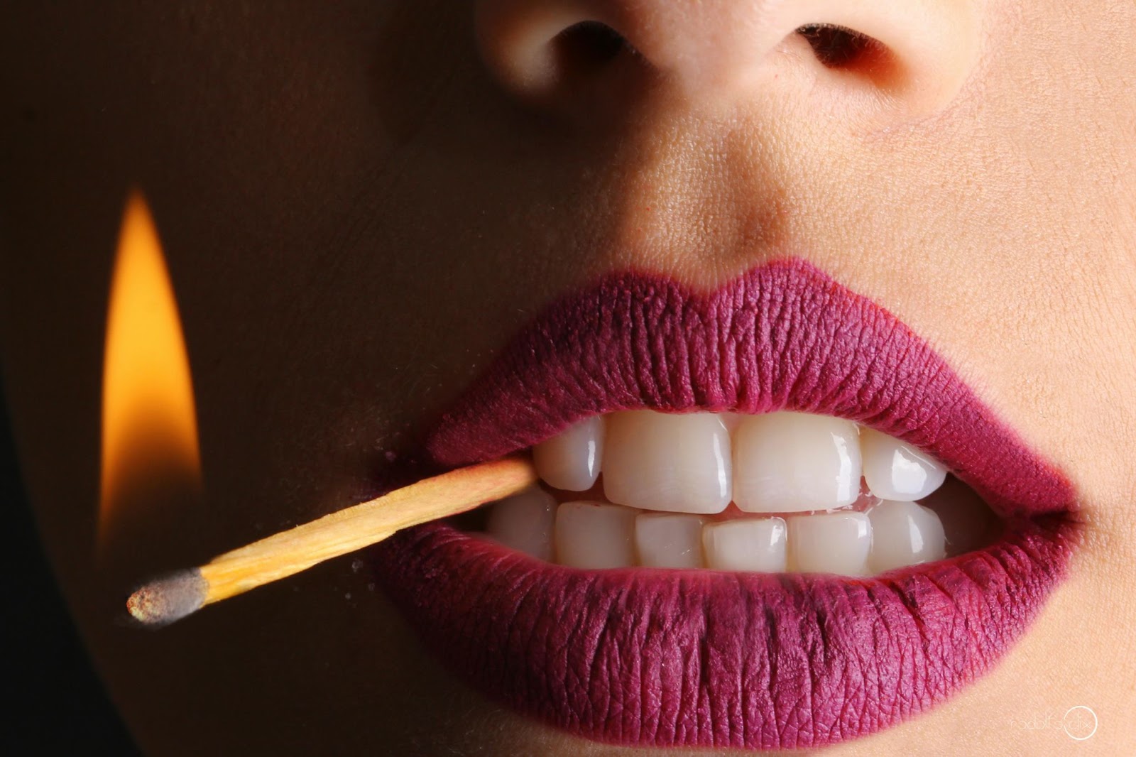 Purple lips holding a burning matchstick