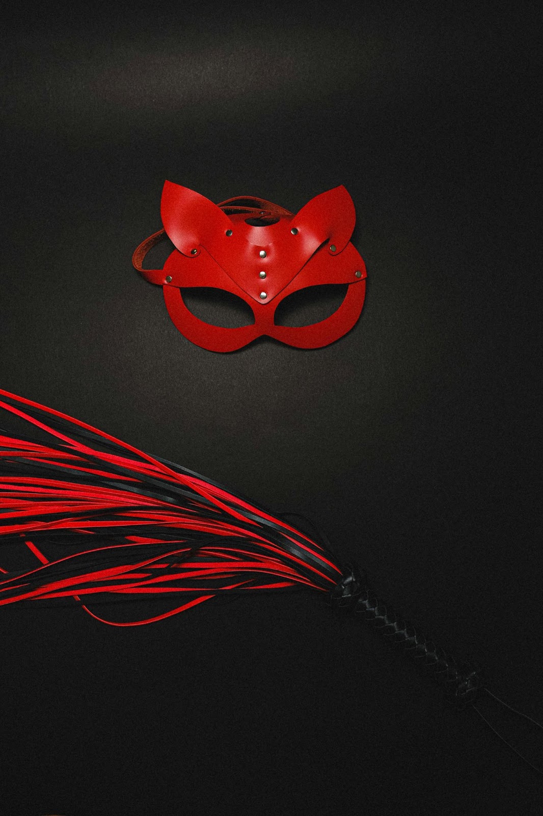 Red leather cat mask and BDSM flogger on black background